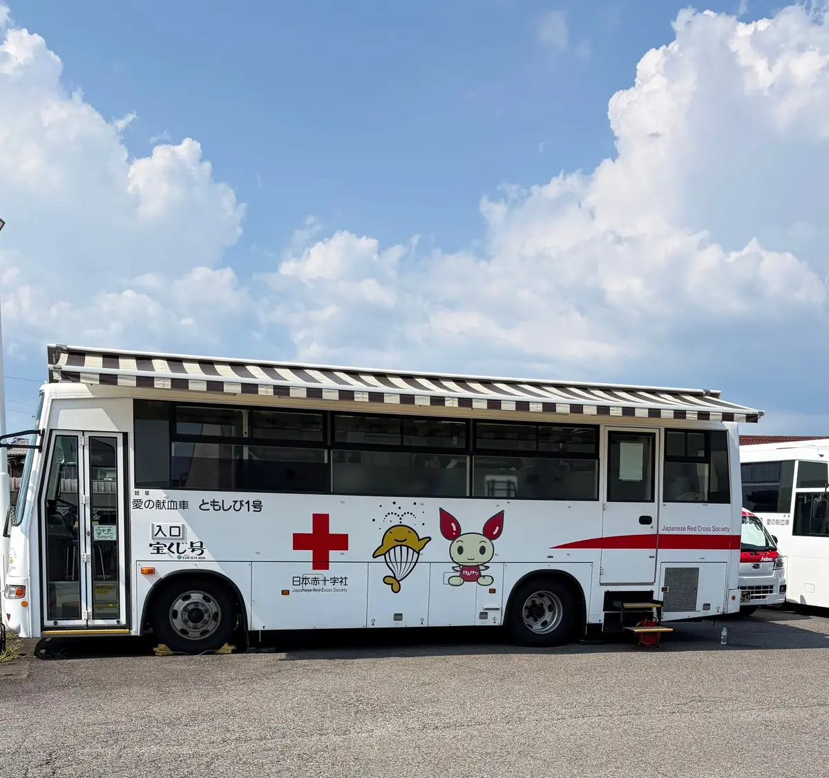 白地に赤十字マークのバス。車体には「日本赤十字社」の文字と、タコとウサギのイラストが描かれている。屋根には日よけのつばがある。