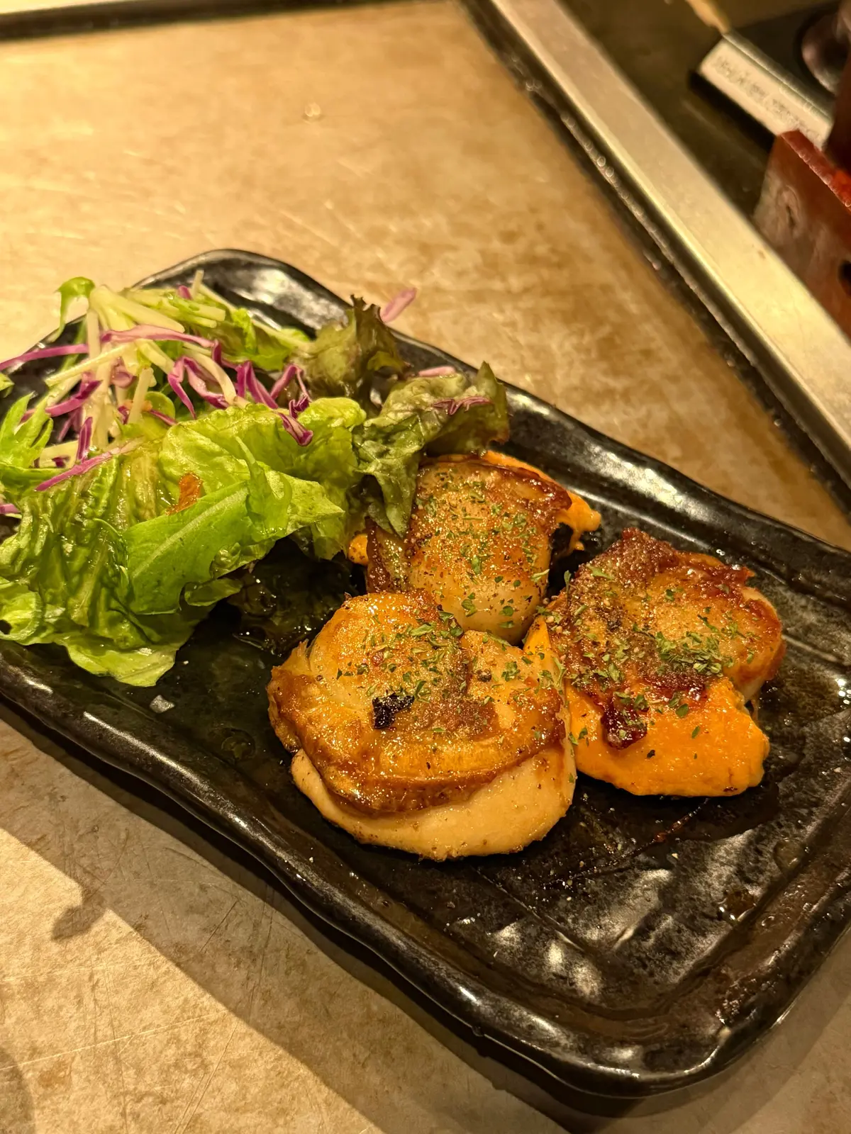 黒い長方形の皿に、照り焼き風味の肉厚なカツ4切れと、レタス、紫キャベツ、赤色の葉野菜を混ぜたサラダが添えられている。