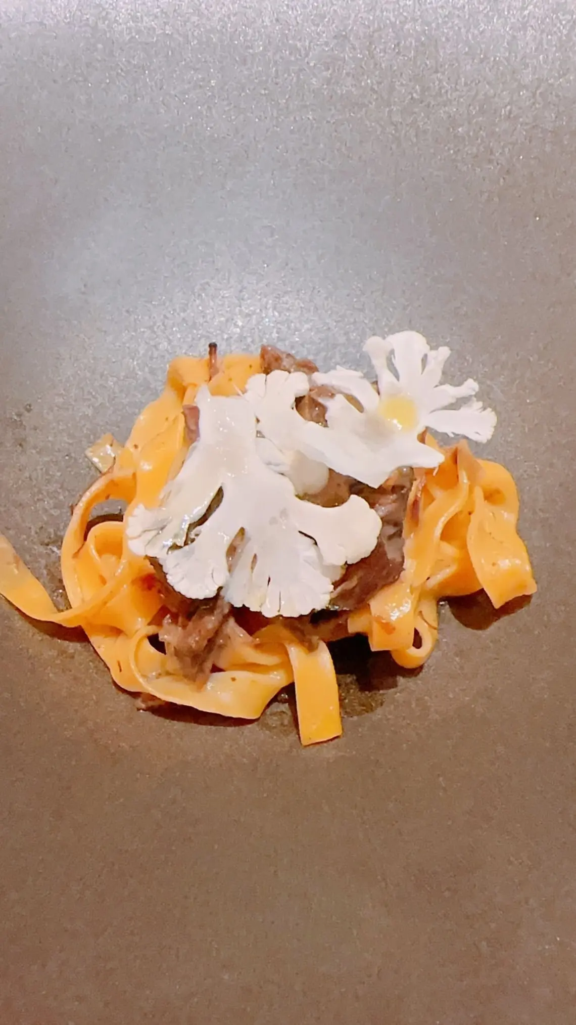 パスタに肉と白い花をトッピングした料理
