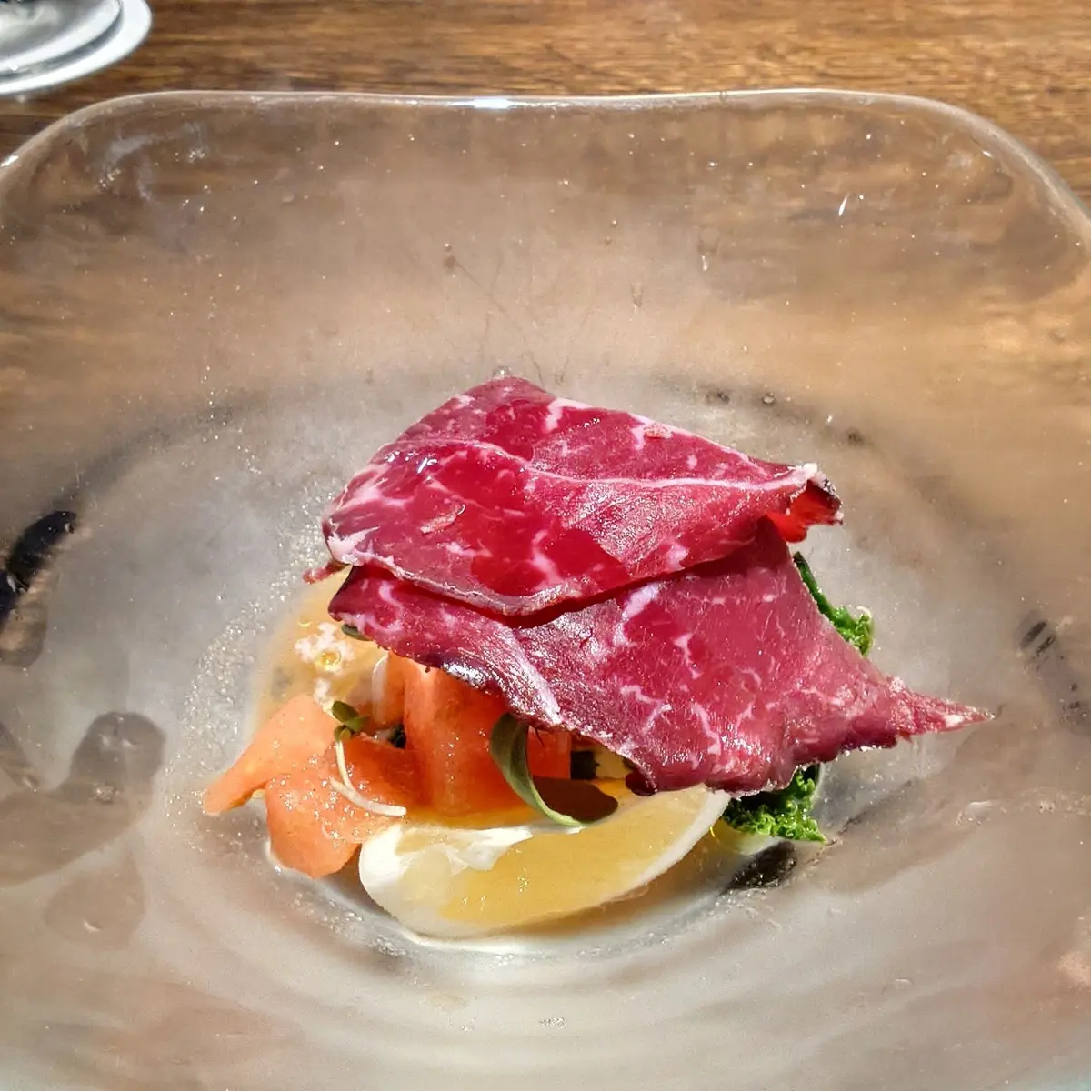 透明な器に盛り付けられた、赤身の牛肉を薄くスライスした料理。西瓜とブッラータチーズのオリエンタル風