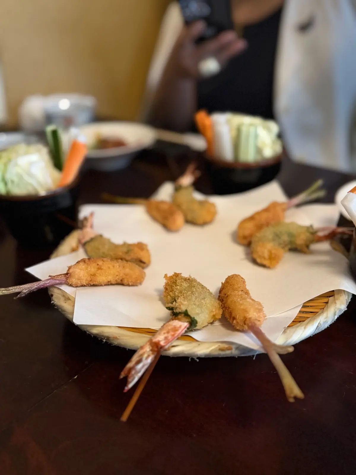 根津、串揚げ「はん亭」、ランチコース、エビと野菜を串に刺した天ぷらが紙ナプキンに並び、周囲にキャベツや人参の副菜が置かれている