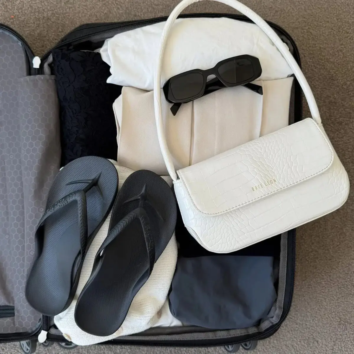白いキャリーケースに、白いバッグ、サングラス、サンダル、白い布などが詰め込まれている様子。Bags Iconのロゴが入った白いバッグが目立つ。
