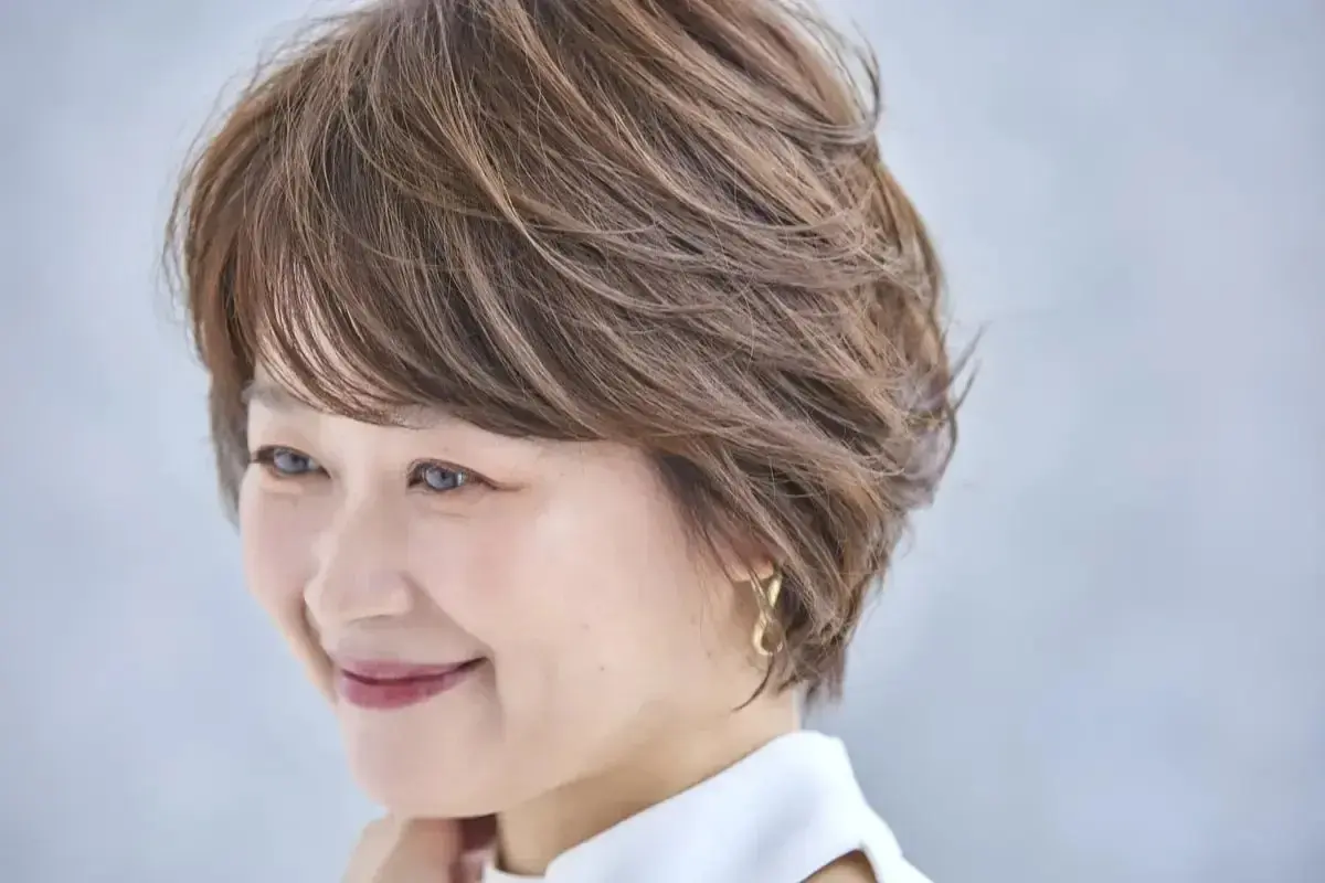 ブラウンのショートヘアの女性が微笑み、ゴールドのイヤリングを着用している
