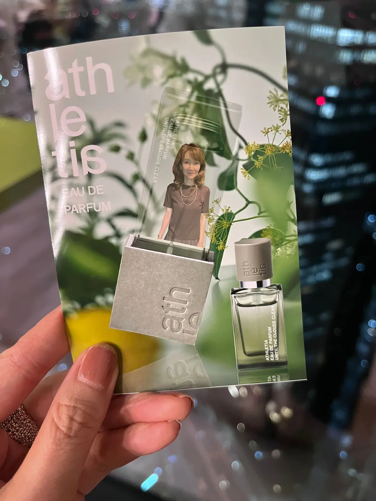 athleitisの香水「Until the Clouds Clear」の広告。背景は淡い色調の植物と女性の写真。手前に香水のボトルと広告カードが置かれている。