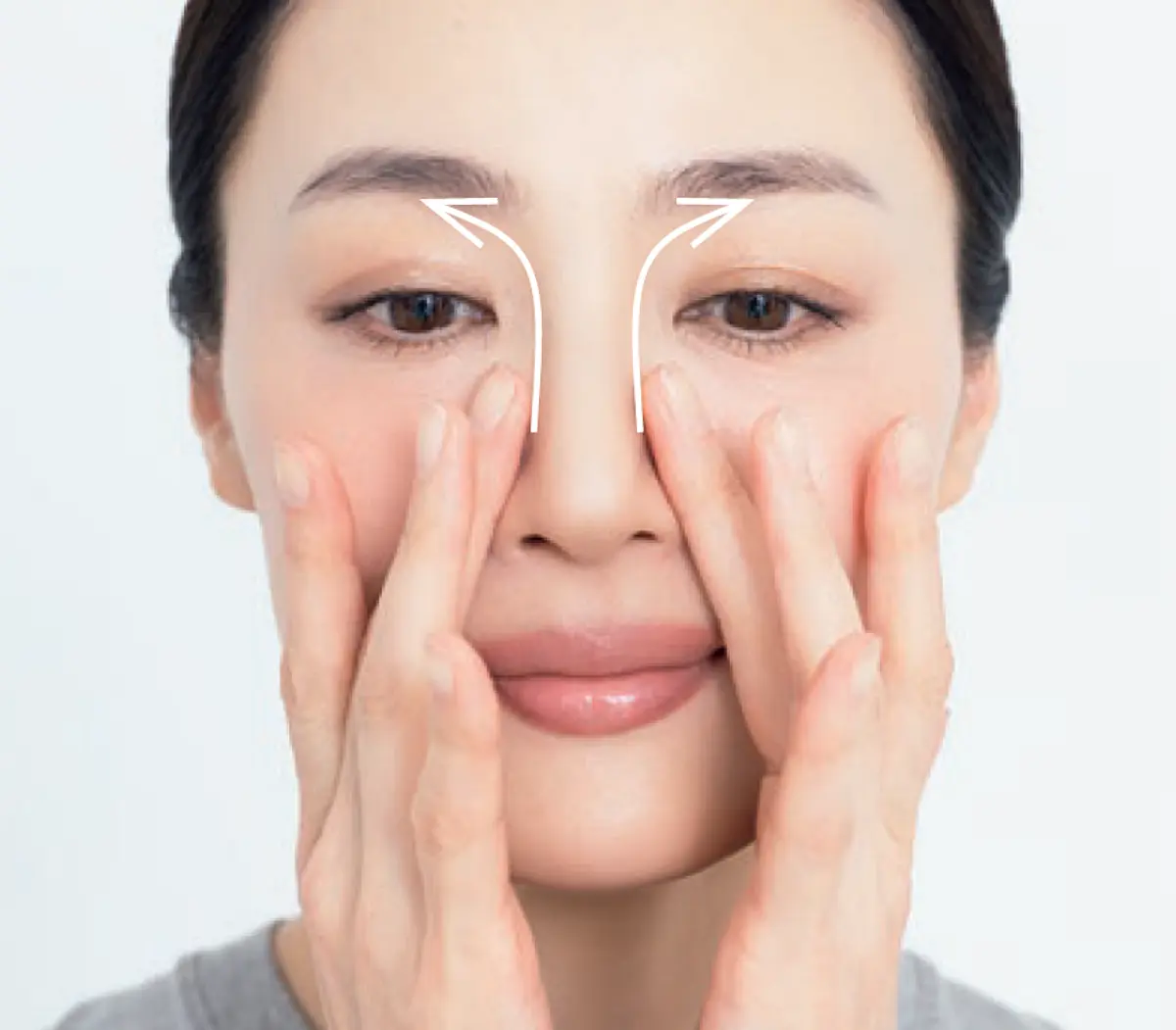 鼻のきわを下から上へ ソフトタッチで流す 両目の外側から眉毛へ向かう白い矢印が描かれた女性が、両手で顔をさすっている