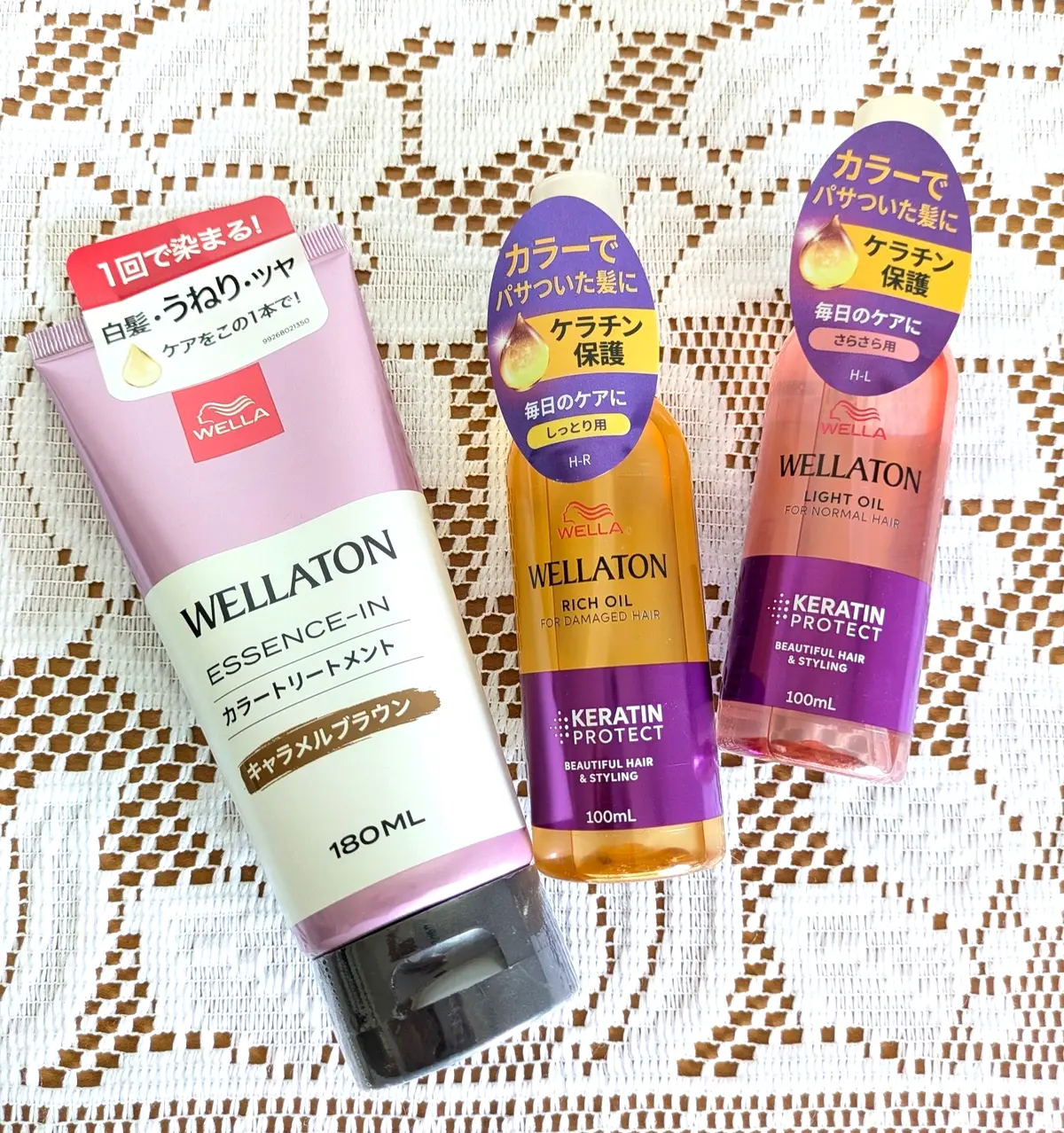 ウエラトーン（Wellaton）のヘアケア製品3点が並ぶ写真。左から、白いチューブ容器に入った180mlのケラチンリートメント、オレンジ色の100mlボトルに入ったリッチオイル、そして黄色の100mlボトルに入ったライトオイル。背景は木目調。