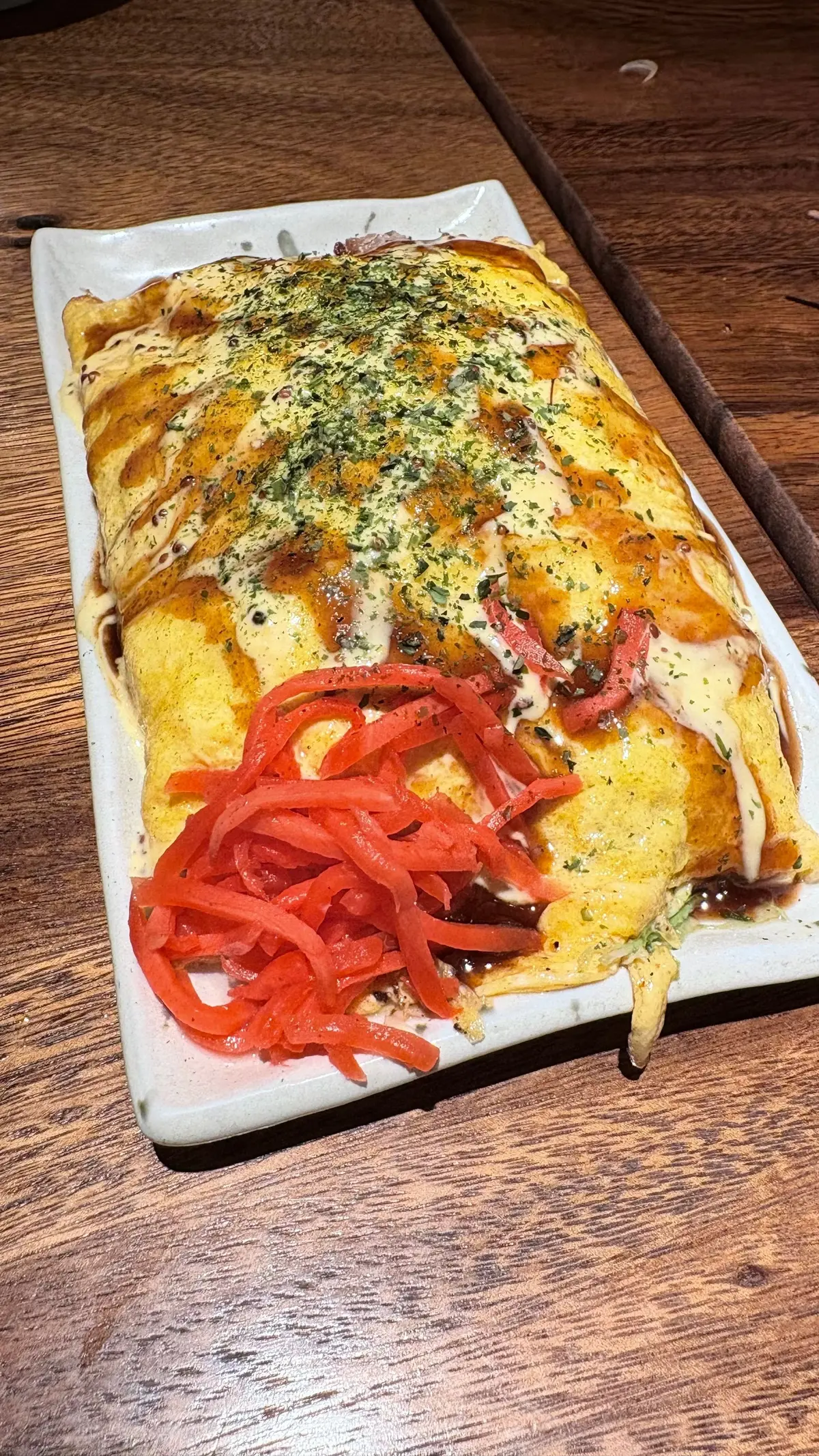 白い長方形の皿に盛り付けられた、卵焼きの上にチーズとソースがかかったオムレツ。赤唐辛子の甘辛い漬物が添えられている。