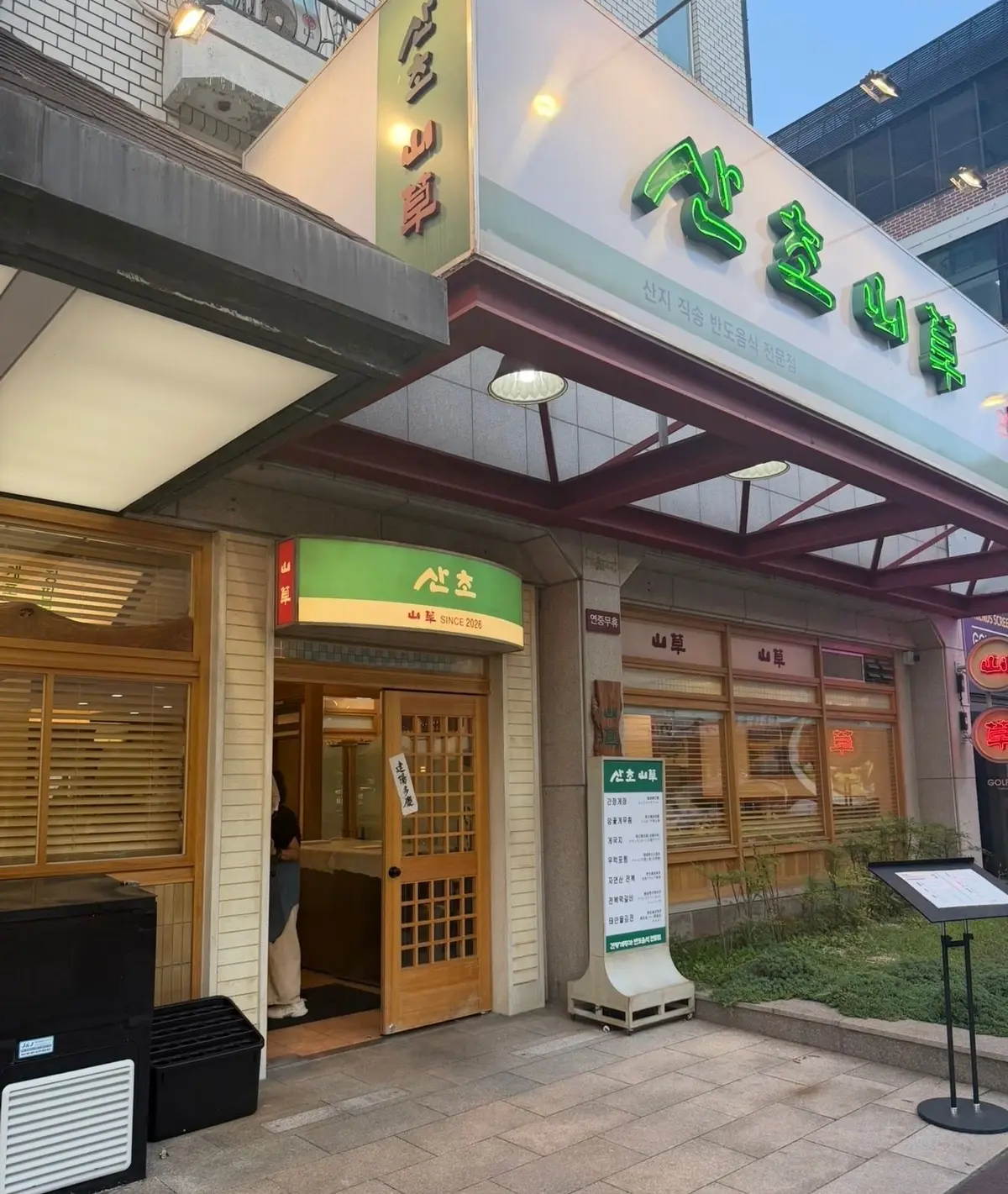 韓国の伝統的な飲食店「산오산」の入り口。緑色の看板と木製のドアが特徴的。看板には「산오산」の文字と「Since 2006」の記載がある。