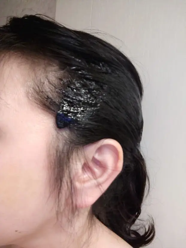 黒髪の女性の側面写真。額から耳にかけて、青と黒のラメ入りのヘアオイルが塗られている。髪は濡れていて、耳の横にうっすらと影が見える。