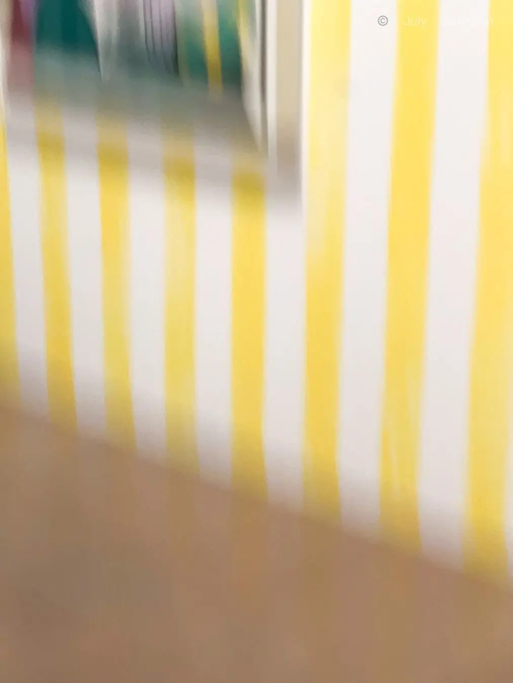 黄色の縞模様が並ぶ背景に、ぼやけた手や物体が映っている。