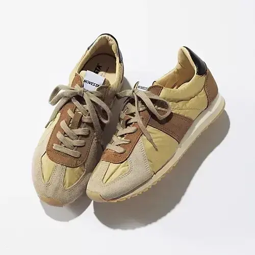 NOVESTAのレトロなランニングシューズ。黄土色と茶色のパネル、黒のアクセント、茶色の紐。左右一対が白い背景に置かれている。