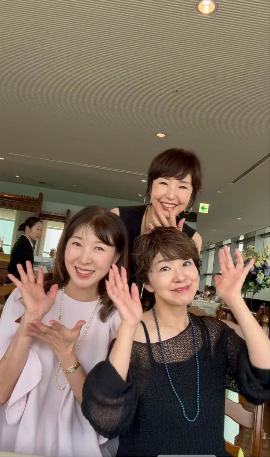 笑顔の3人の女性が手を振って写っているセルフィー写真。背景には窓から光が差し込む明るいレストランが見える。