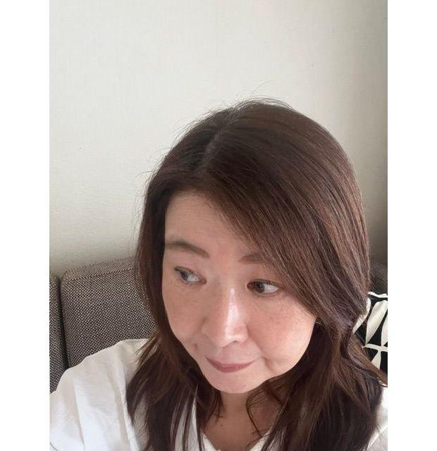 茶色の髪の女性が、白いシャツを着てこちらを見ているポートレート。背景は白っぽい壁とグレーのソファ。