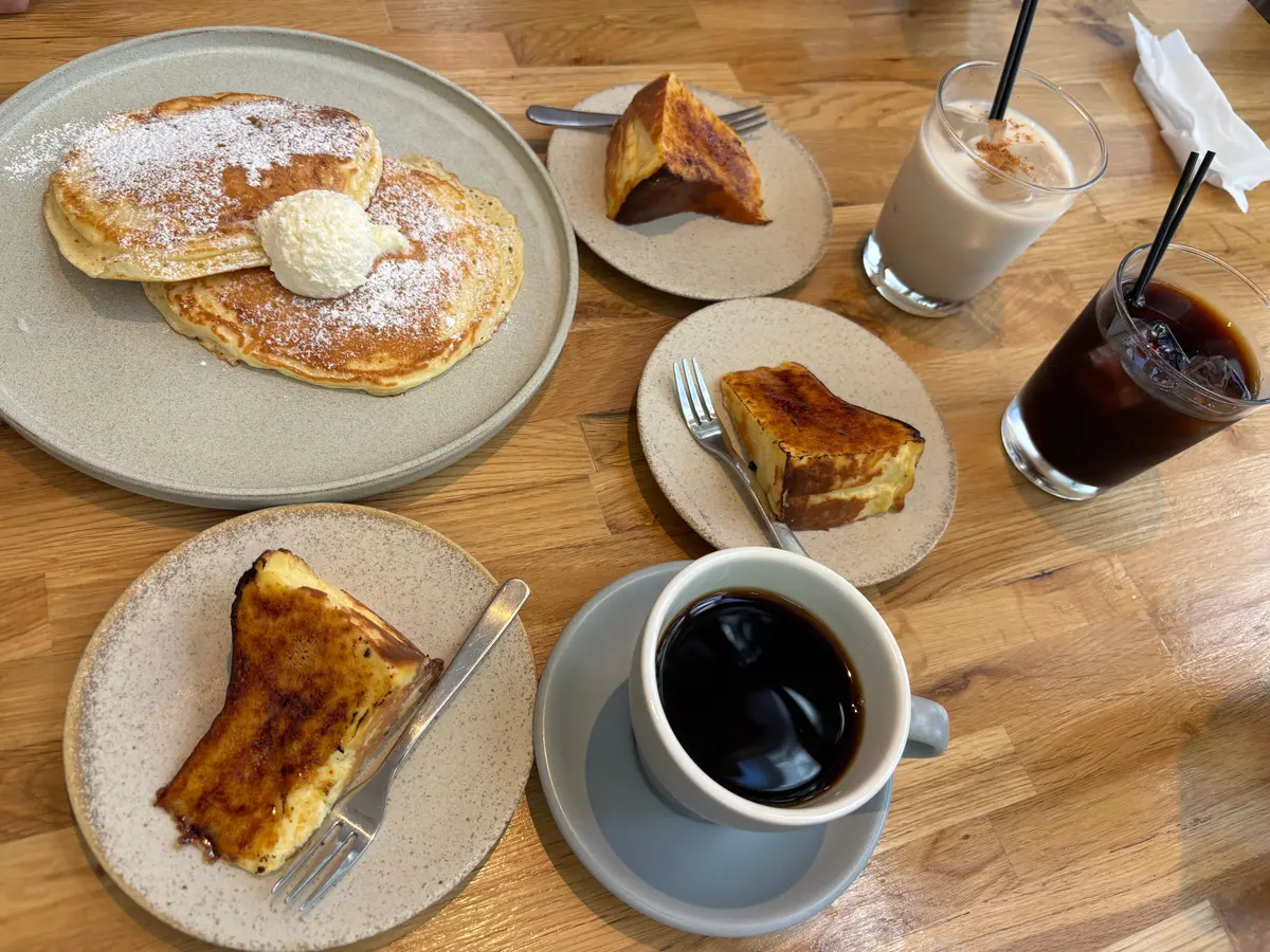 粉砂糖をまぶしたパンケーキとアイスクリーム、トースト、ミルクとコーヒーの飲み物が木製テーブルに並ぶ