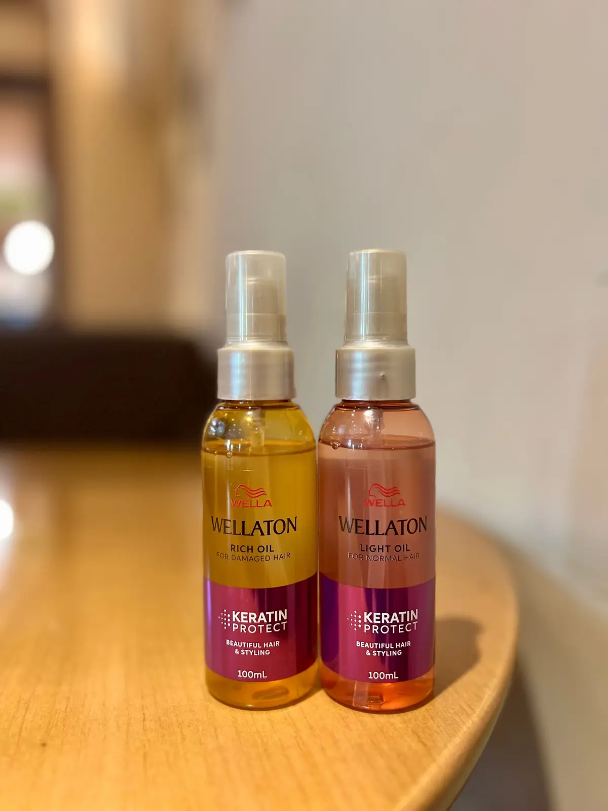 Wella Wellatonのヘアオイル2本。左はオレンジ色の「ダメージヘア用」、右はピンク色の「ノーマルヘア用」。どちらも100mlのボトルで、白いプッシュ式キャップが付いている。