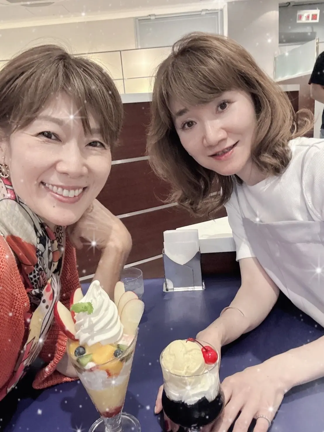 二人の女性がテーブルに座り、フルーツとアイスのデザートを前に笑顔でカメラに向かっている。
