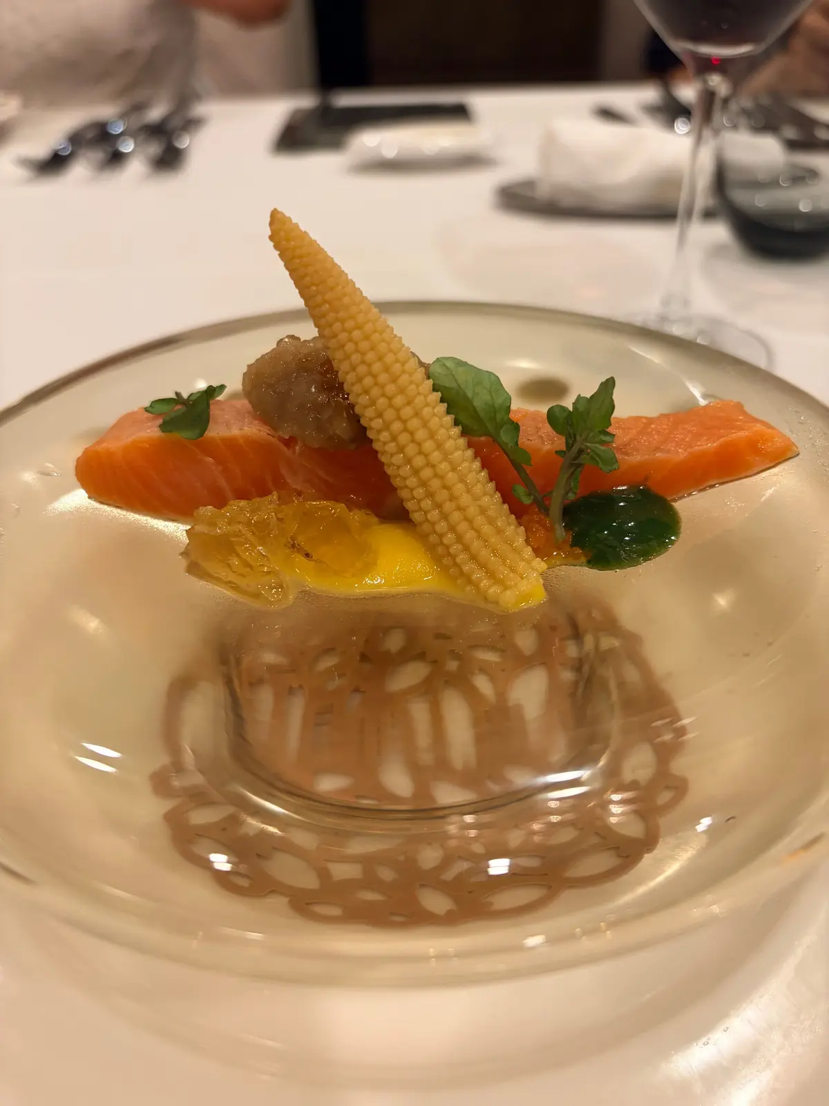 白磁の皿に盛り付けられた、サーモンのパイ生地料理。オレンジ色のサーモン、黄色いコーン、緑の葉が彩り、茶色のソースが描かれている。