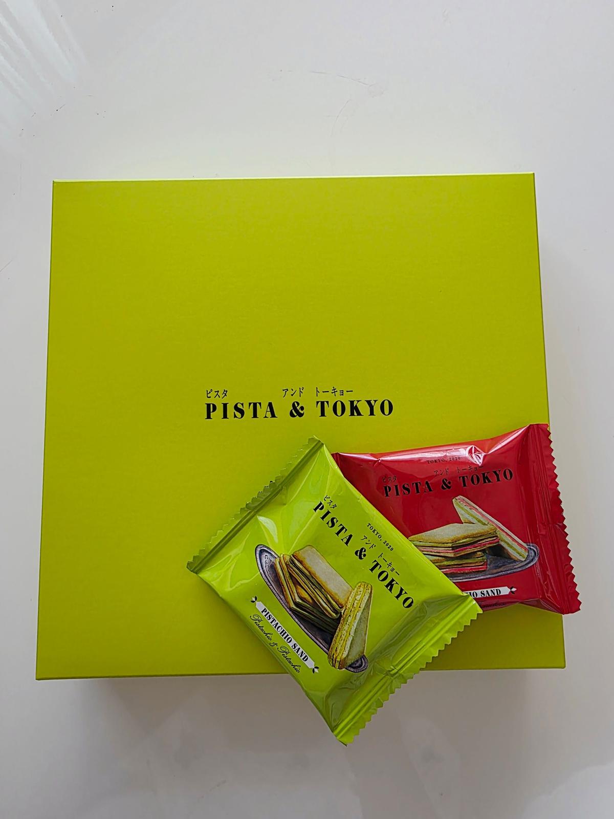 鮮やかな緑色の箱の上に、ピスタ＆トーキョーの個包装されたお菓子が置かれている。緑、赤、茶色のパッケージが並び、それぞれにブランド名と商品名が記載されている。