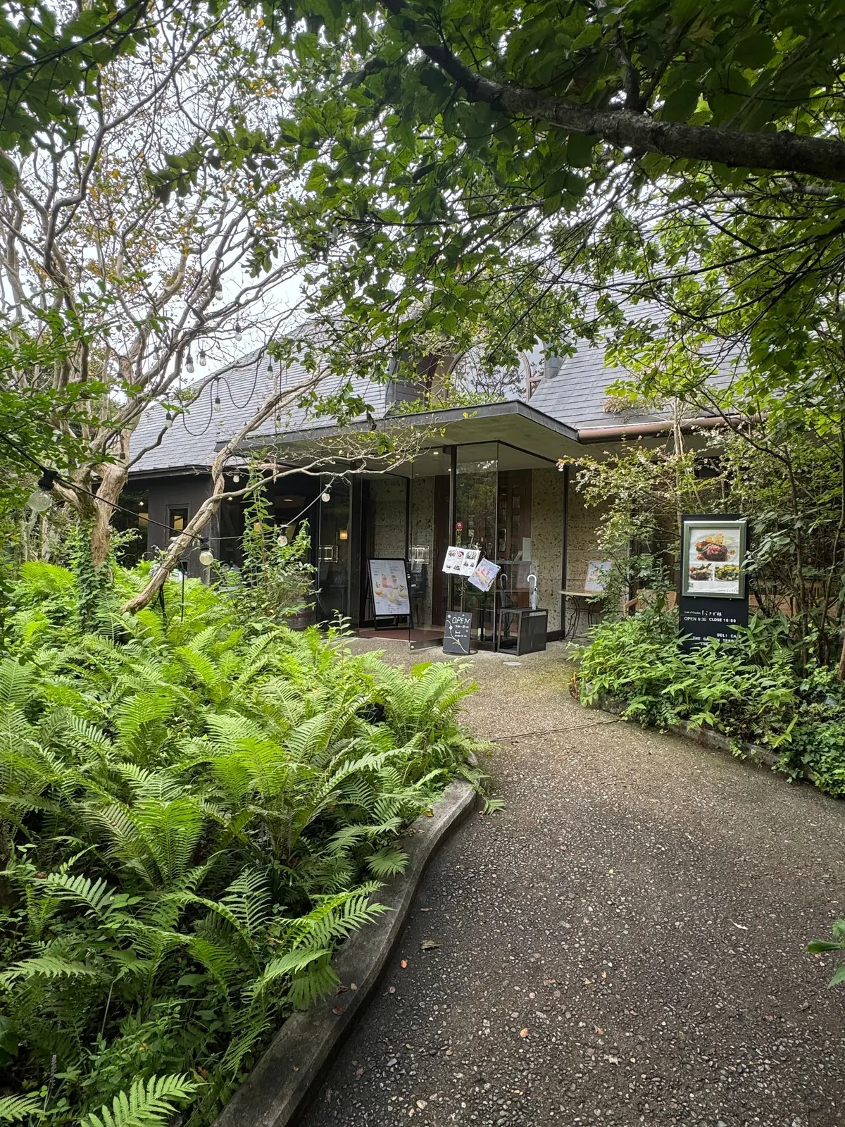 緑豊かな植栽に囲まれた、木造のレストラン。石畳の小道が建物へと続いており、入り口付近にはメニューなどが書かれた黒板が置かれている。