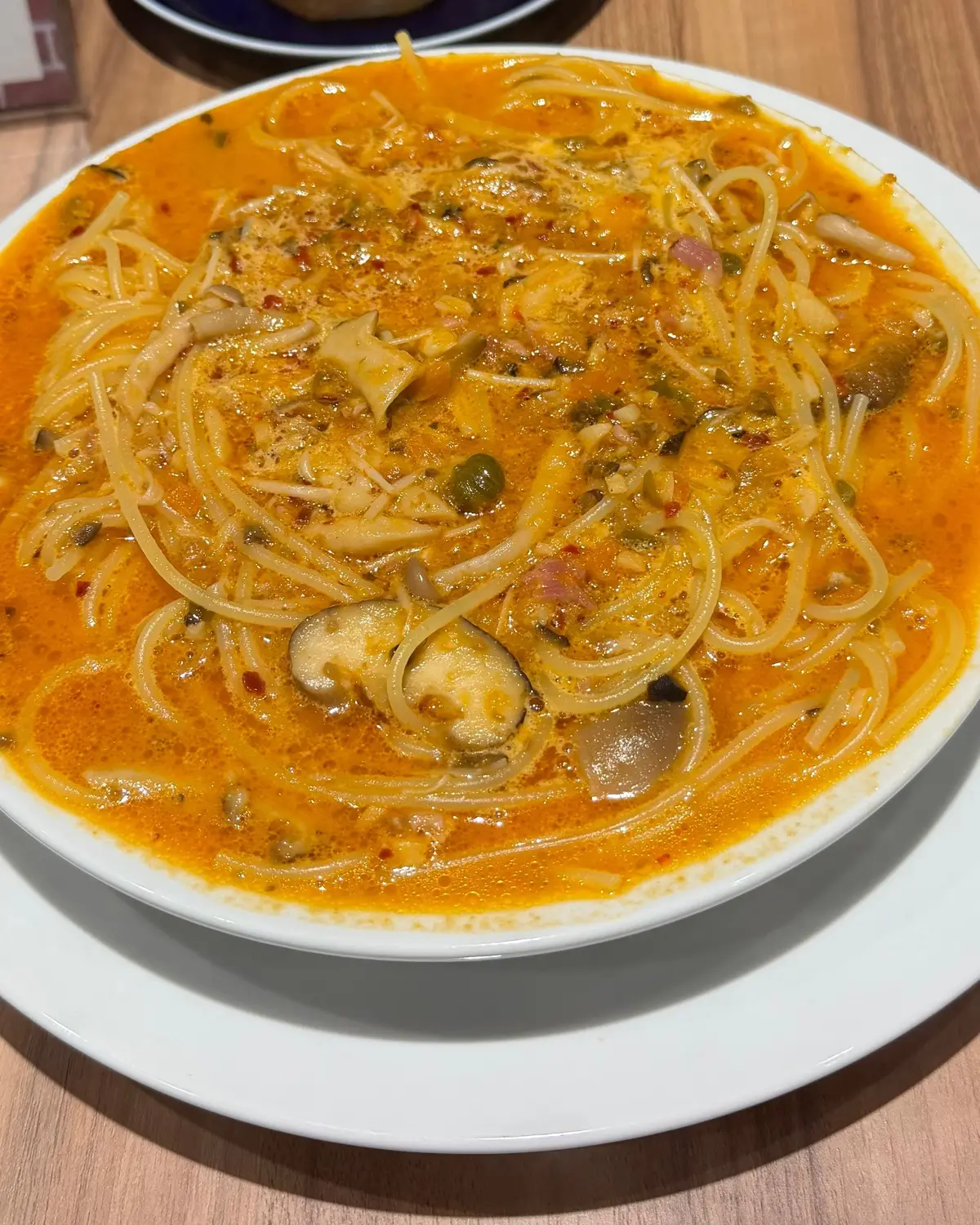 白い皿に盛り付けられた、オレンジ色のパスタ料理。スパゲッティと、カシューナッツ、きのこ、トマトなどの具材が混ざり、表面にはハーブや赤唐辛子が散らされている。