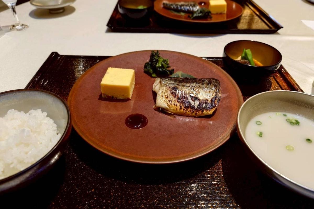 漆塗りの長方形の木製プレートに盛り付けられた和朝食。中央にはグリルされた鯖、その横には卵焼き、緑色の野菜、ご飯、そして粕汁が置かれている。