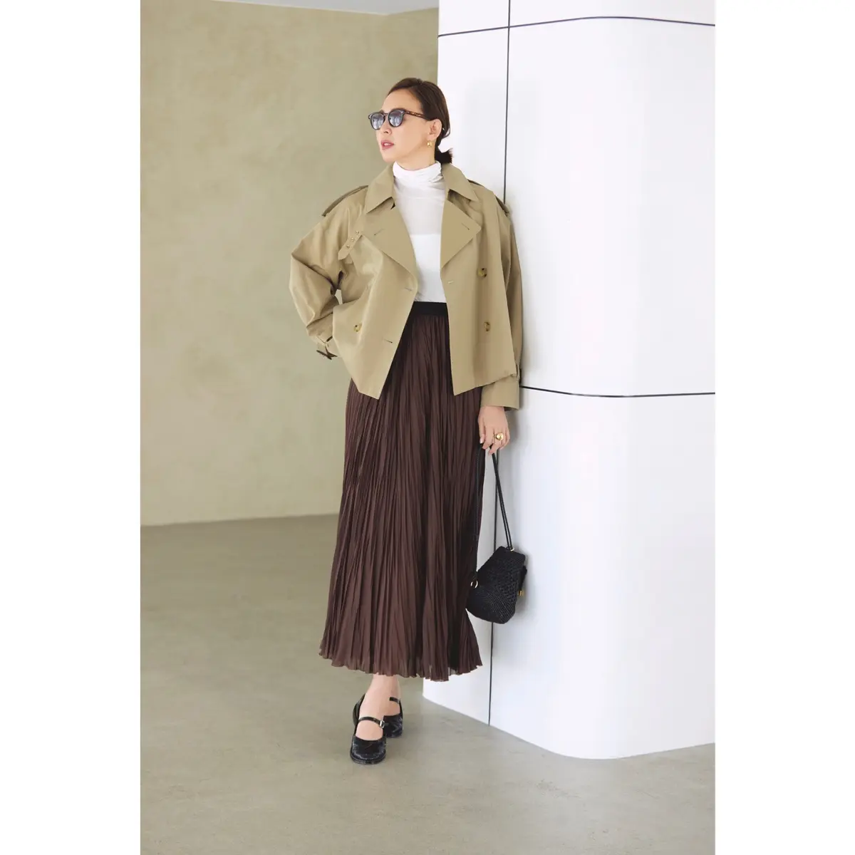 白ハイネックトップスにブラウンプリーツスカートを合わせ、上からショート丈のベージュトレンチコートをはおったコーディネート　モデル・SHIHO