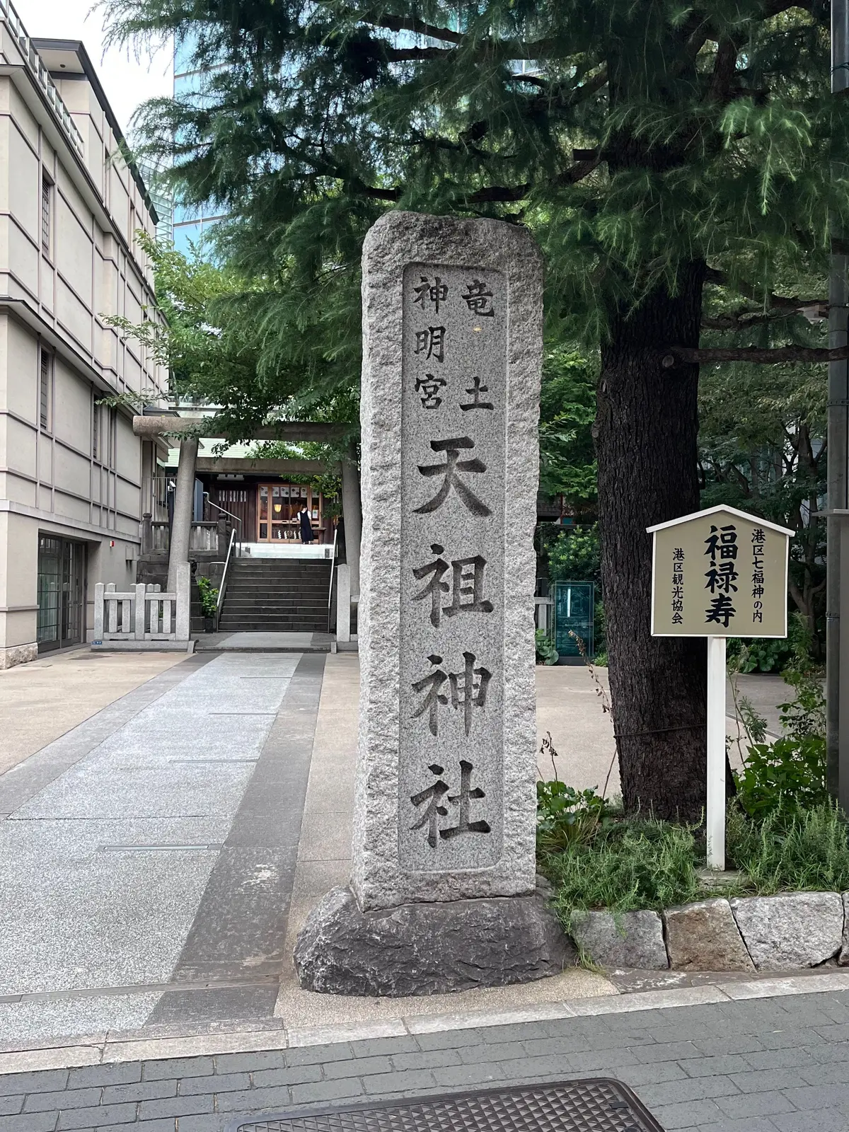 石柱に「上明宮天祖神社」と墨書された看板と、その奥に見える階段と社殿。緑豊かな木々に囲まれた神社の入り口。