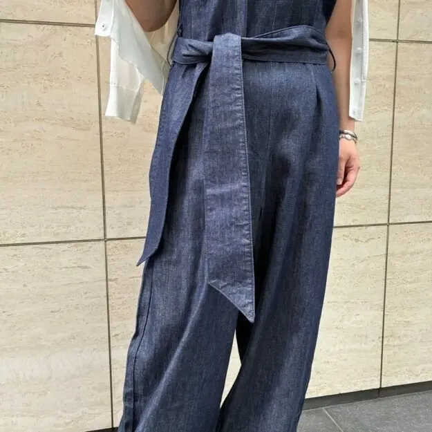濃い青色のデニム素材のワイドパンツ。ウエストには長めのベルトが巻き付けられ、前で結ばれている。白いシャツを合わせている。
