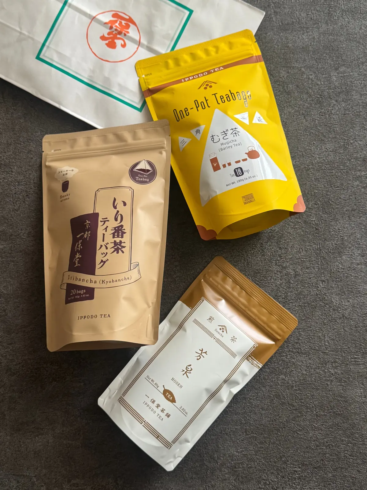 茶葉ティーバッグ3種が並んでいる。左は茶色のパッケージで「イリバンチャ（キョウバンチャ）」と表記、中央は黄色で「むぎ茶（バレイティー）」、右は金色の袋で「ロゼン茶」と記載されている。