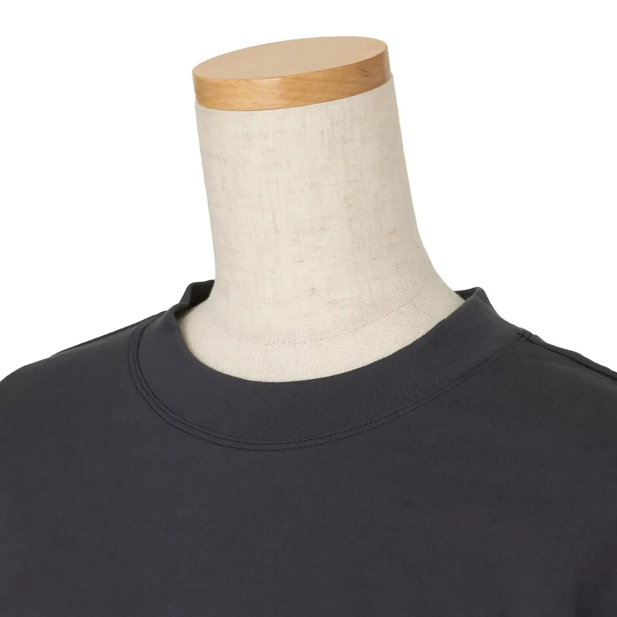 黒色のクルーネックのTシャツ。木製の台にセットされており、首元から肩にかけて写っている。シンプルなデザインで、無地である。