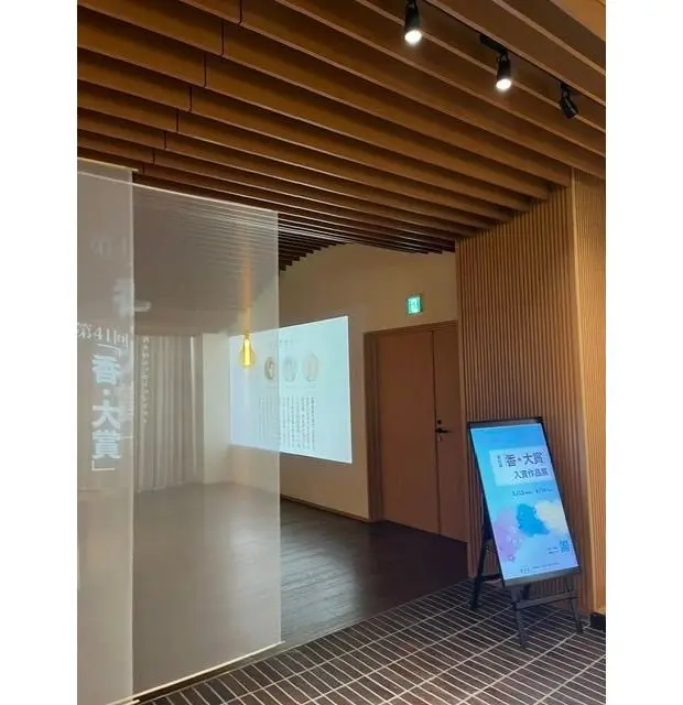 木製の天井とフロアが敷かれた展示スペース。スクリーンに情報が表示され、右側に立ったパネルに「水辺の旅」が書かれている。