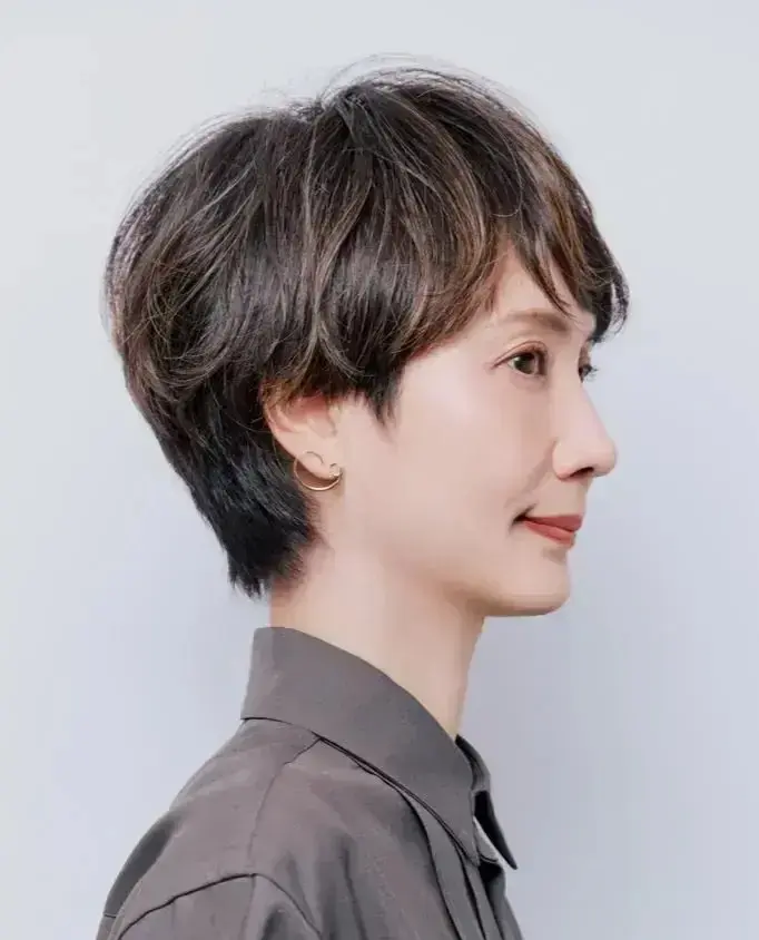 ショートヘアの女性が左を向いて微笑み、ゴールドのイヤリングを着用している