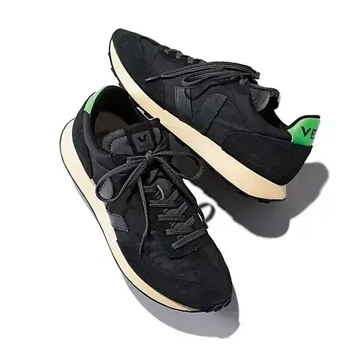 黒いスエード素材の Veja（ヴェジャ）のランニングシューズ。白のソールと、緑色のアクセントが施されている。左右一対が置かれている。