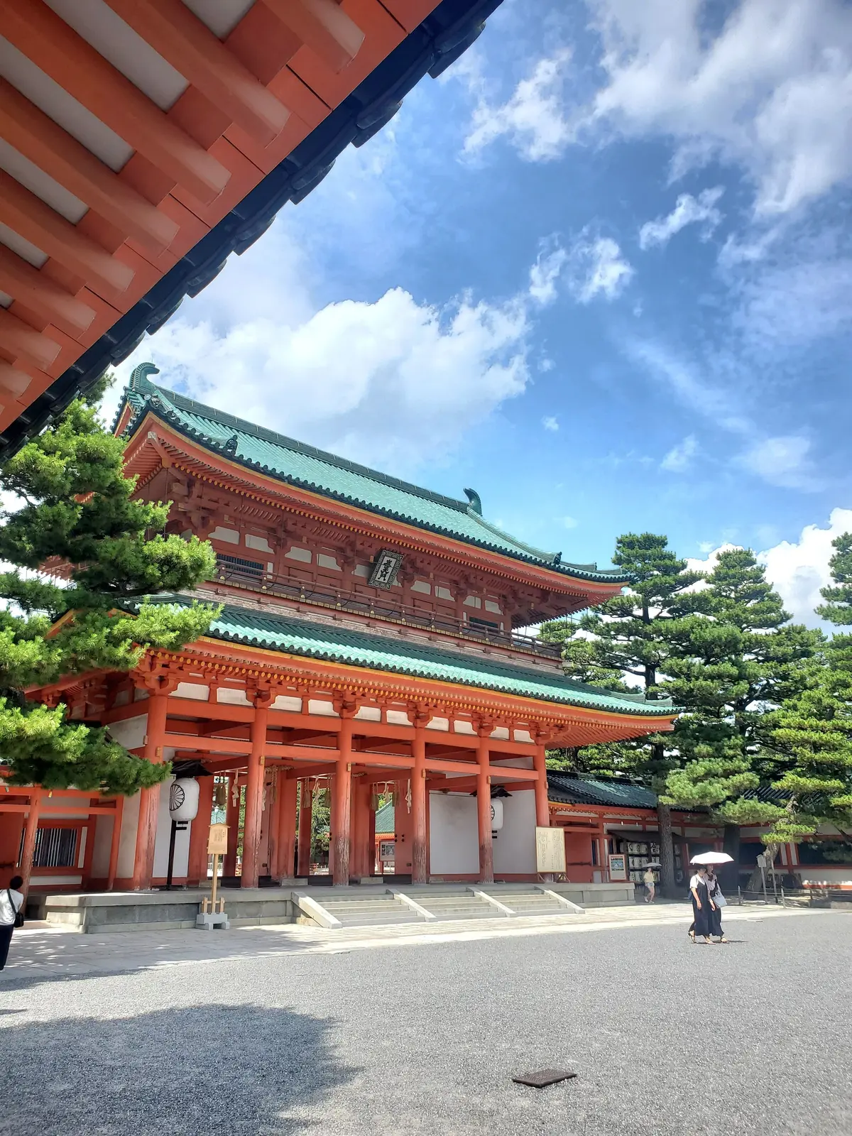 鮮やかな朱色の楼門と緑色の屋根が特徴的な日本の寺院。晴天の空の下、石畳の広場に佇む姿を捉えた写真。
