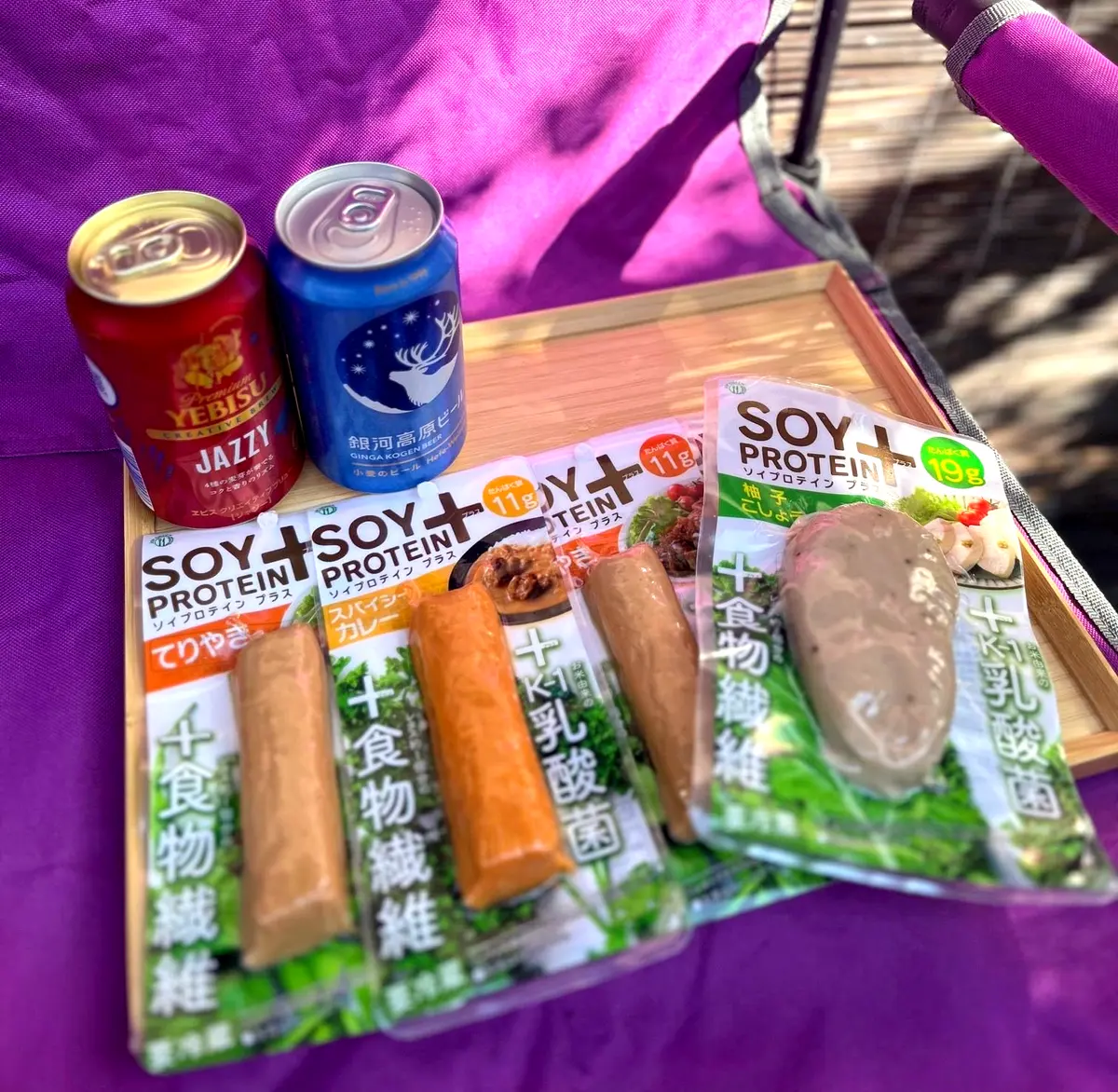 木製のトレイに、サントリーのYebisuビール、Soy Protein＋が4種類が置かれている。背景には紫色のシートが写っている。
