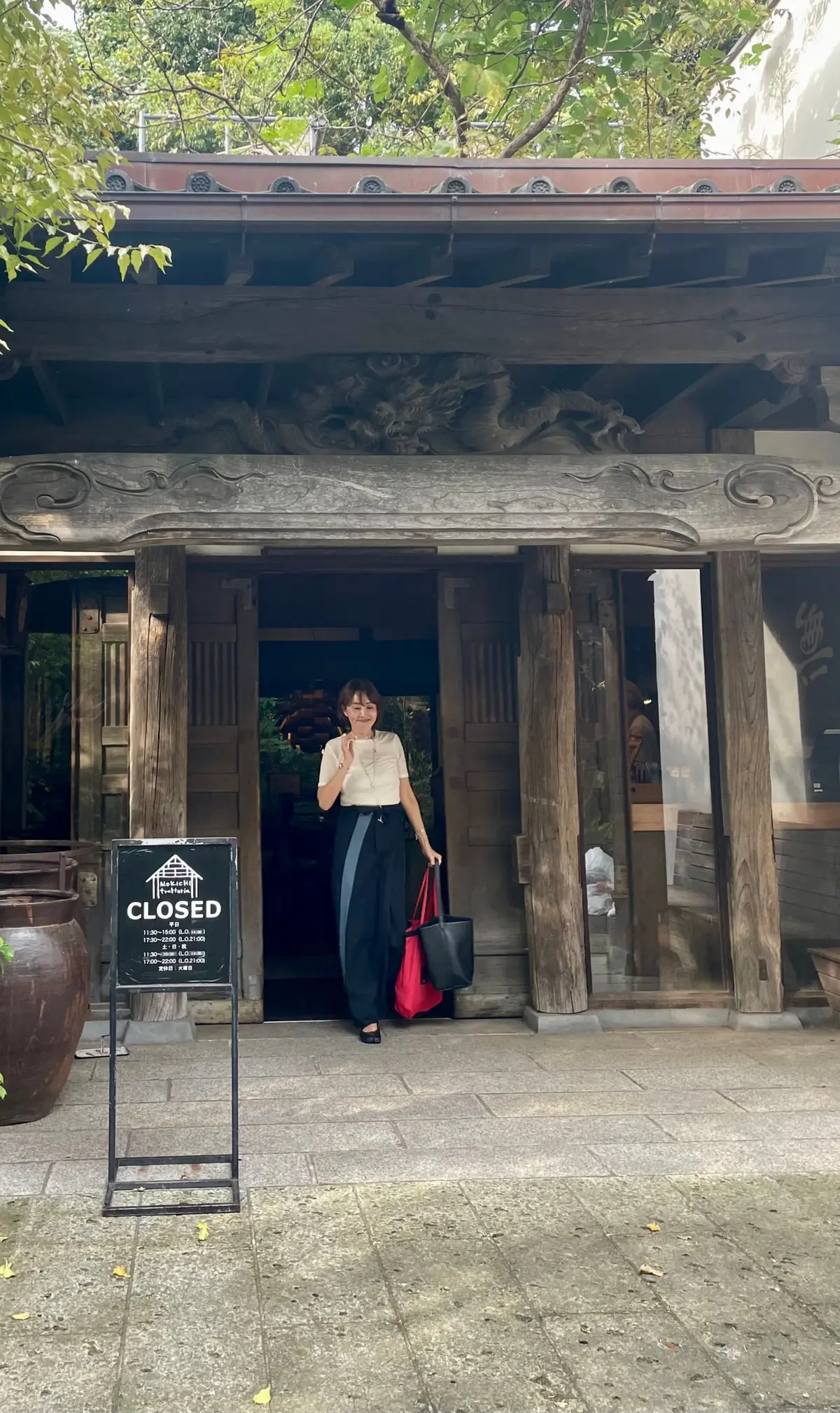木造の伝統的な建物。入り口に「閉館」の看板が置かれ、女性が立ち入る様子。建物は木の色で統一され、屋根には装飾がある。背景には緑豊かな木々が見える。