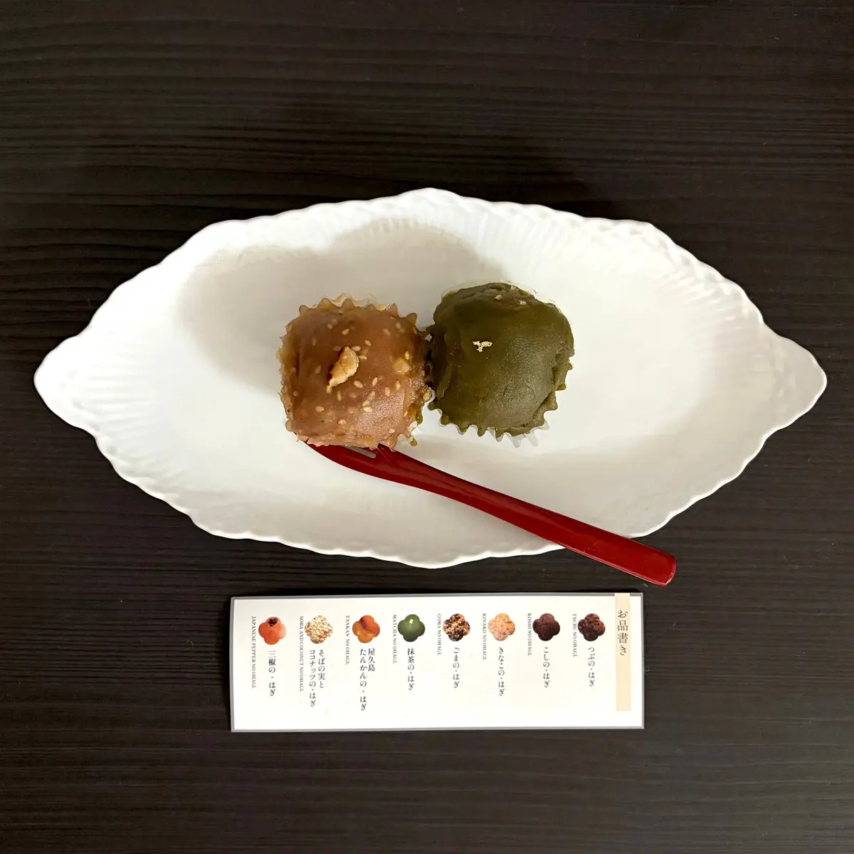 白い皿に、みたらし胡桃、抹茶味のおはぎが２つ並んで置かれている。下には、和菓子の紹介文が書かれた紙が添えられている。