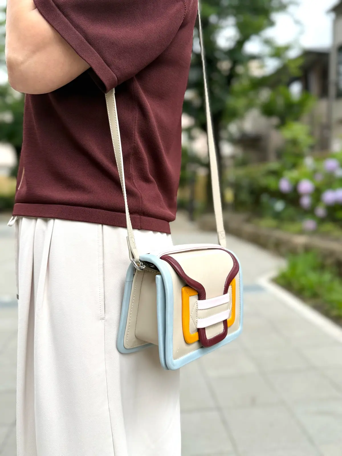 ピエールアルディー、マロンブラウンのトップスとベージュのスカートを着た人物が、ベージュとライトブルーのショルダーバッグを斜め掛けしている