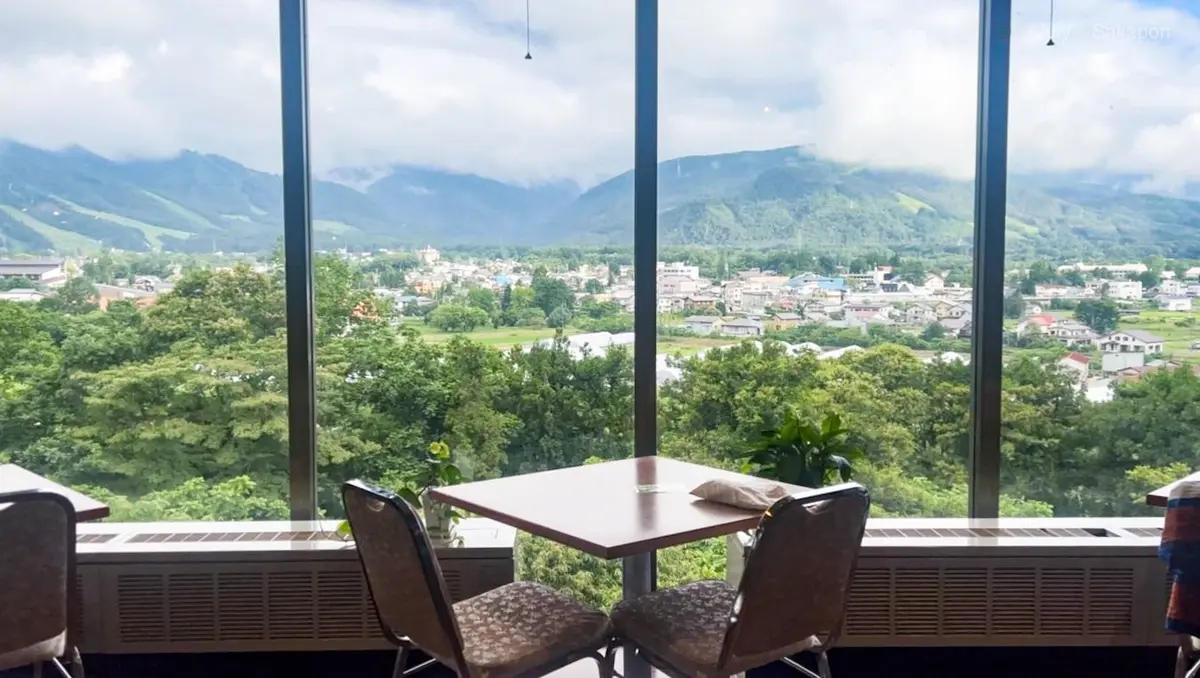 窓から見える山と街並みの景色、木製テーブルと椅子が配置された明るい部屋