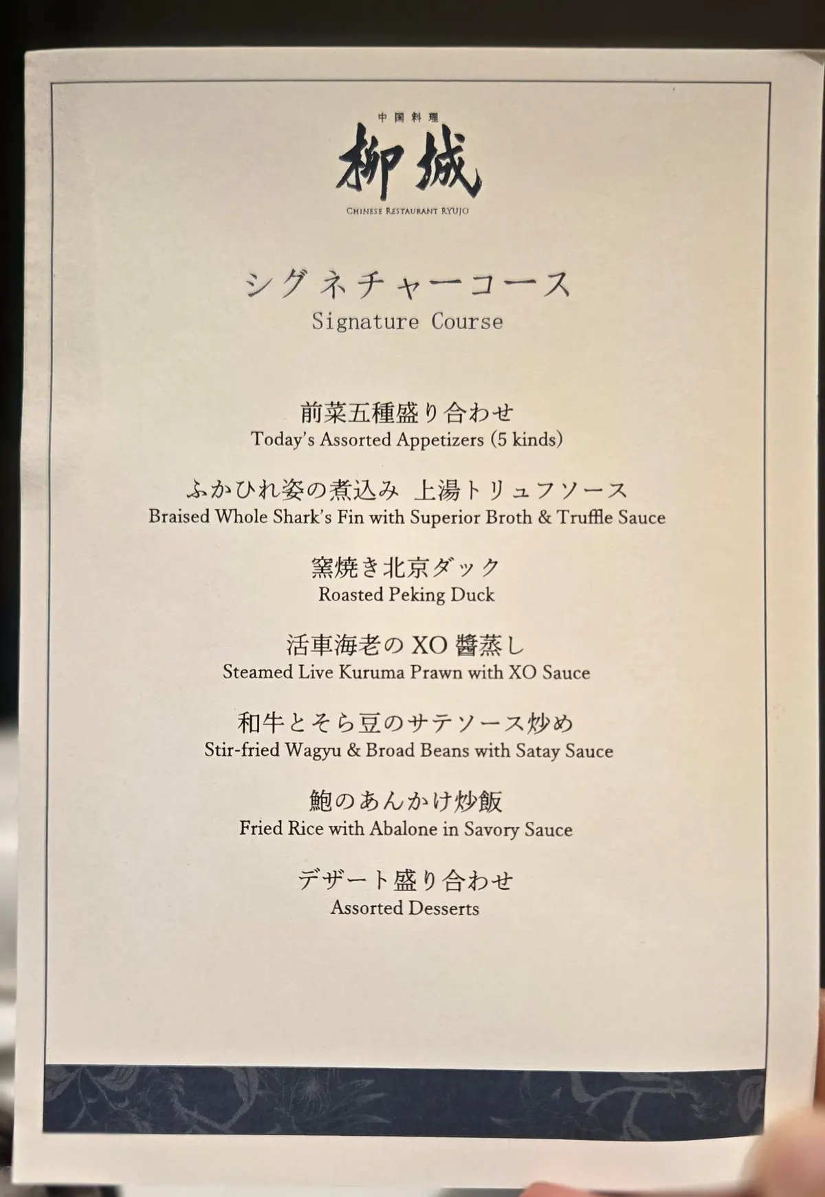 中国料理店のメニュー。黒地に白文字で「都城」のロゴと「Signature Course」のタイトルが記載。その下に、前菜五種盛り合わせ、北京ダック、エビ料理、ご飯料理、デザートのメニューが日本語で列挙されている。
