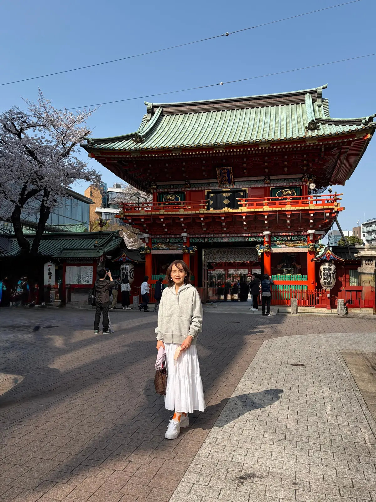 桜満開の神田明神の前で写真を撮る女性
