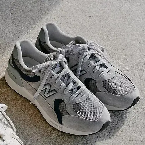 グレーのスニーカーがペアで置かれている写真。New Balanceのロゴが側面に見える。シューレースは白、ソールは白とグレーの組み合わせ。