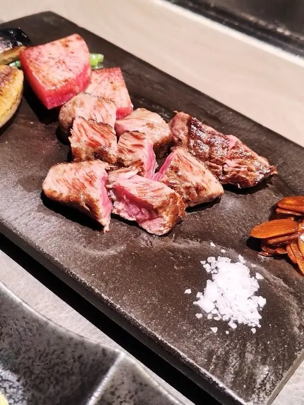 黒い長方形の皿に、赤身と白身のコントラストがはっきりとした牛肉の塊が並んでいる。右下には塩が振りかけられ、右端には炒めたきのこが添えられている。