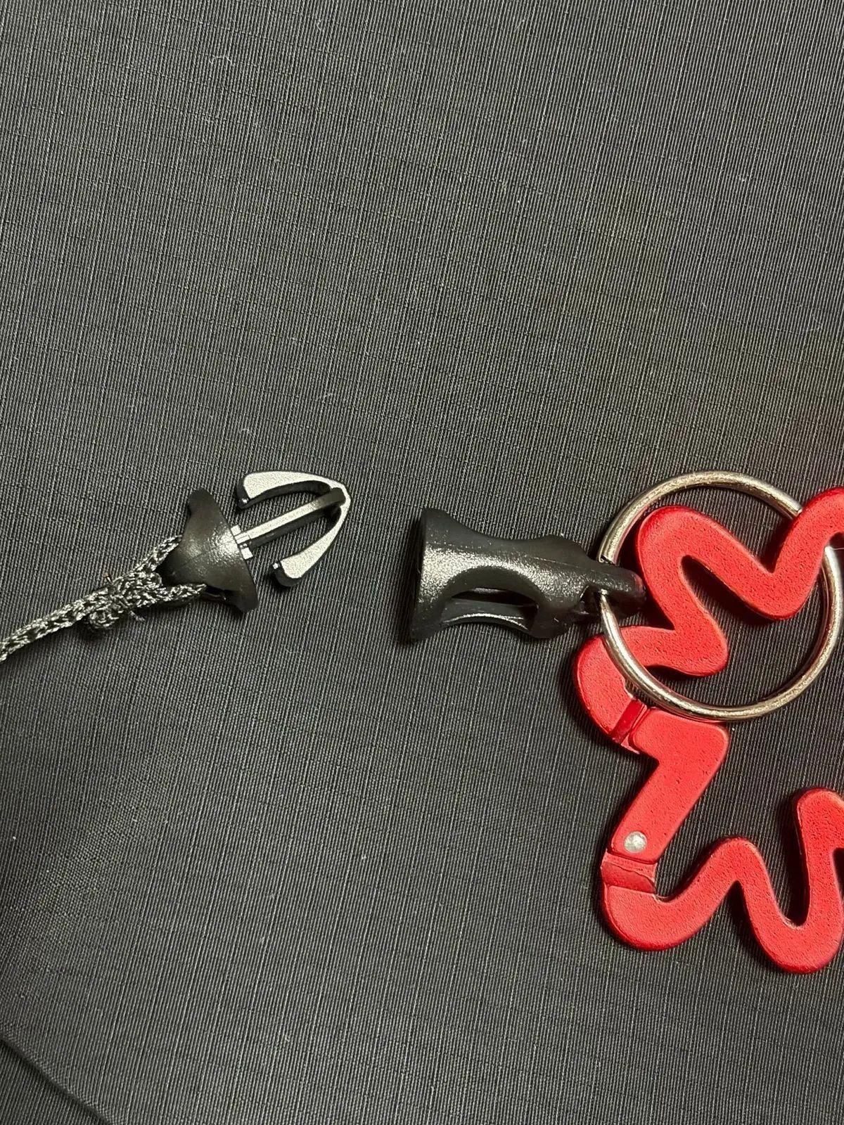 グレーの生地の上に、黒いジッパー引き手、黒いバッジ、赤と白の渦巻き模様のキーホルダーが置かれている。