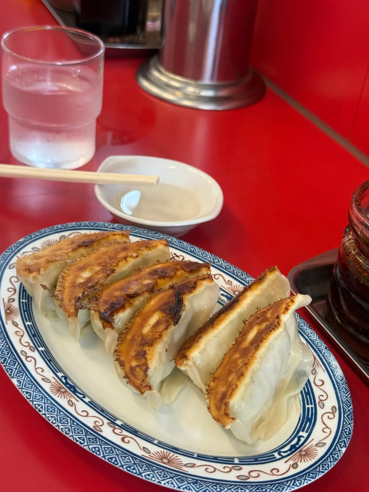 赤いテーブルに青と白の模様のある皿に、焼きぎりぎりの天ぷら風の餃子が並んでいる。ガラスの飲み物と白い小皿も見える。