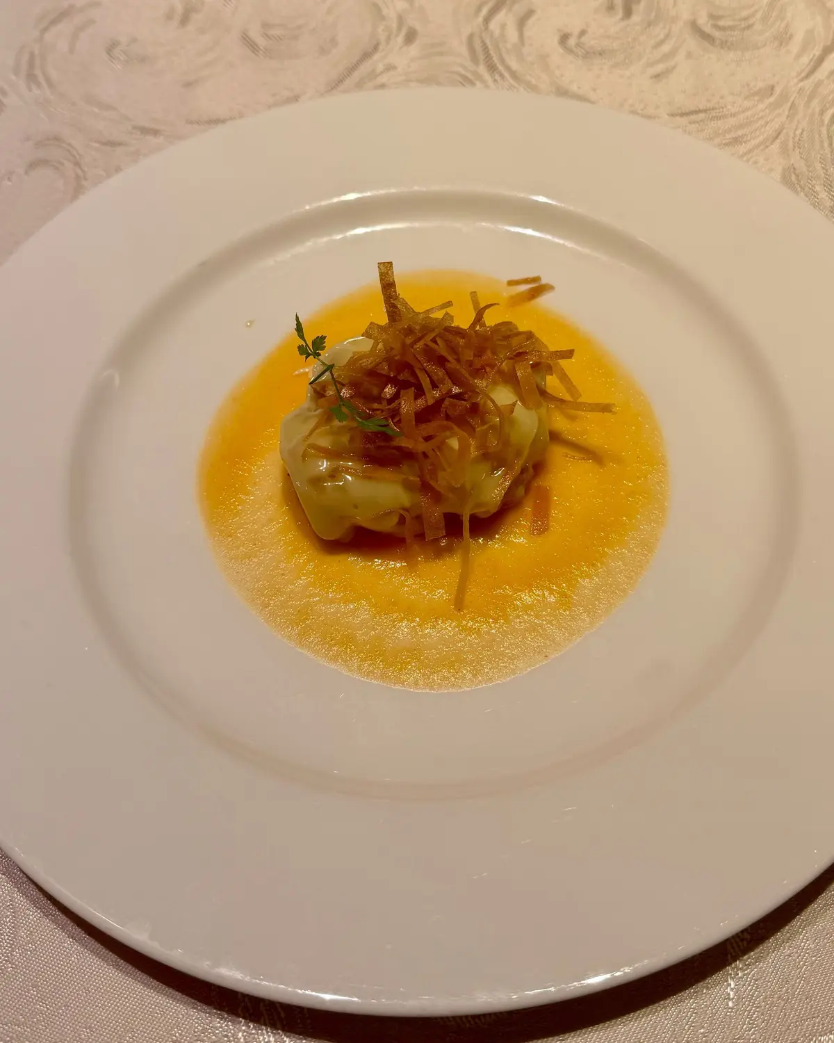 白い皿に黄色のソースを敷き、中央にクリーム状のもの、細切りの野菜とハーブがトッピングされた料理