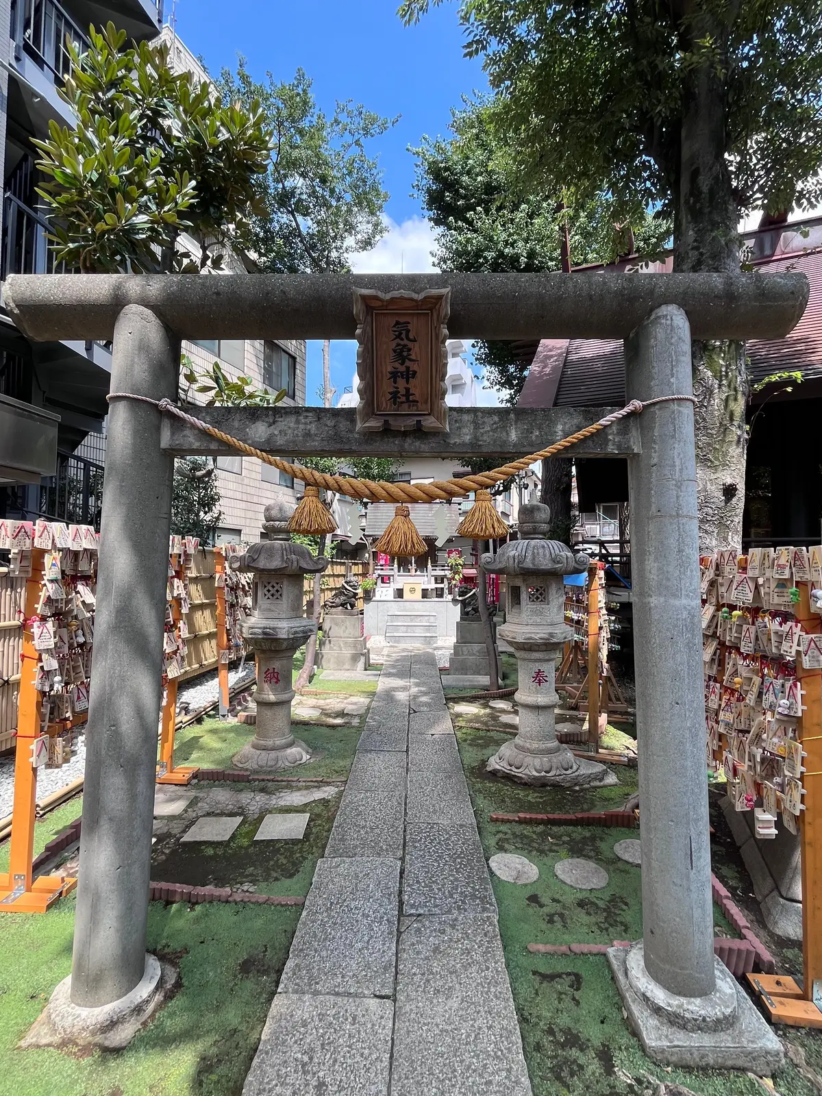 鳥居が設置された神社の参道。左右に石灯籠が置かれ、背景には木々と建物が見える。鳥居には漢字で書かれた額が掛けられている。