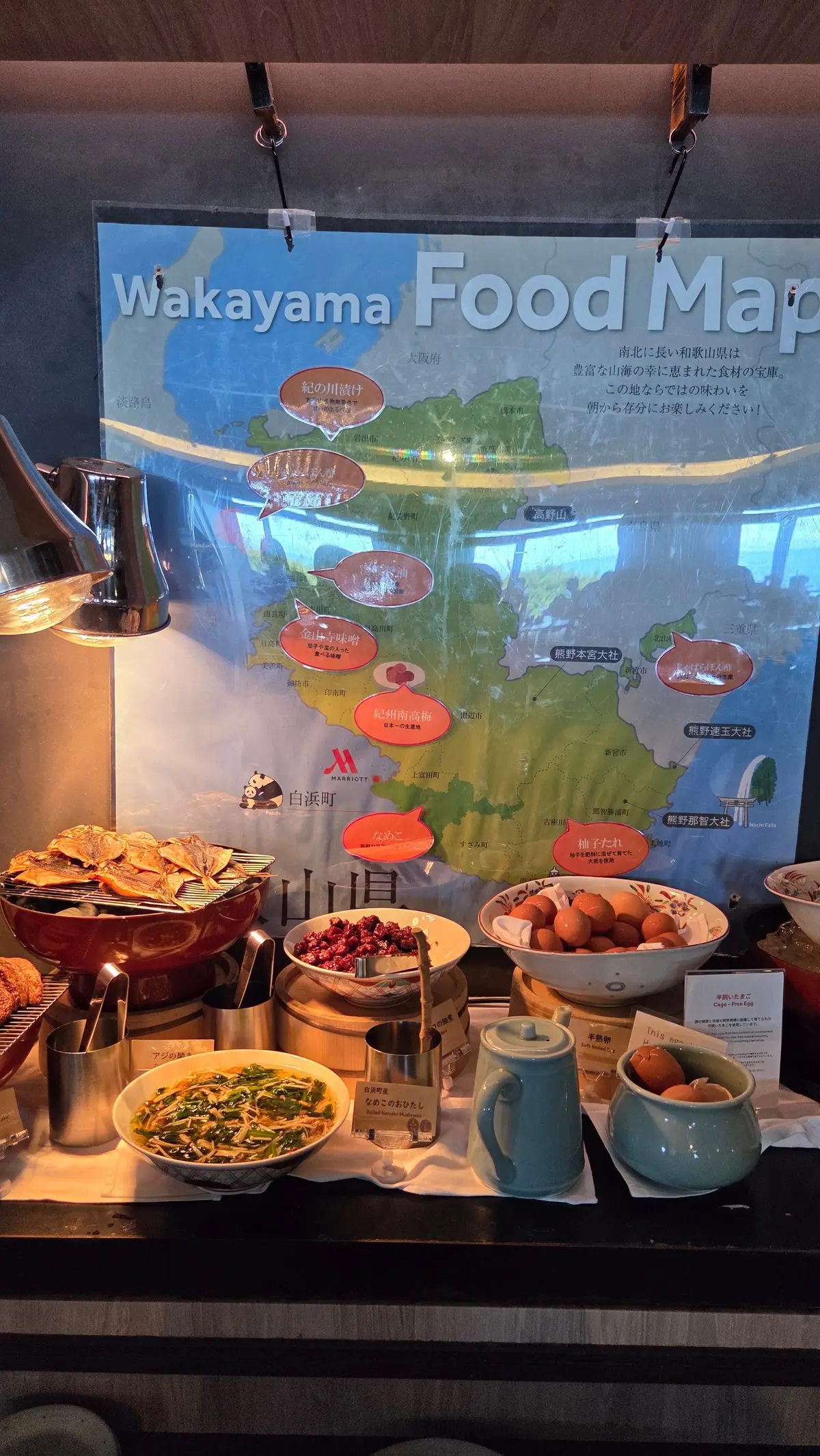 和歌山県の食マップが飾られたビュッフェ台。様々な料理やフルーツ、飲み物が並び、温かい照明が当たっている。