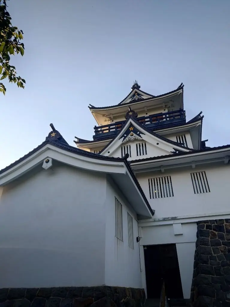 白漆喰の城郭と、紺色の屋根瓦が美しい城の天守閣。多層構造で、各層に金色の星の装飾が施されている。石垣が基礎部分を囲んでいる。