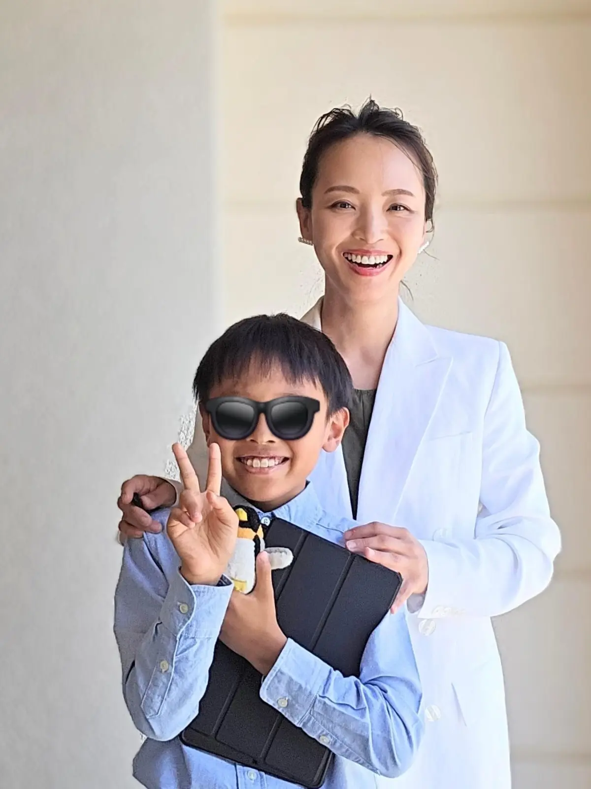 笑顔の女性と少年。女性は白衣を着用し、少年はサングラスをかけている。少年はタブレットを持ち、女性に寄りかかっている。背景はクリーム色の壁。